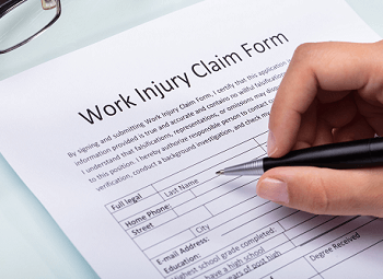 hand holding a pen to fill out a work injury claim form