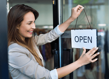Woman small business owner puts up an open sign on the front door of her storefront